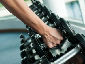 Arm with hand reaching down and grabbing a dumbbell from a rack of weights for article Top 8 Phoenix Area Gyms for newcomers moving to Phoenix.