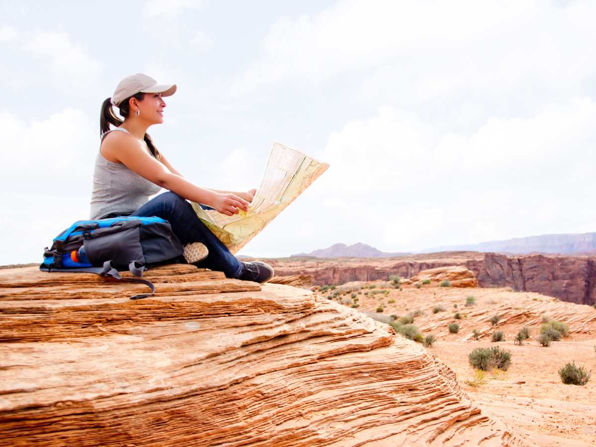 Woman sitting cross legged with a map overlooking Grand Canyon for article Arizona is one of the top states people are moving to for newcomers moving to Arizona.