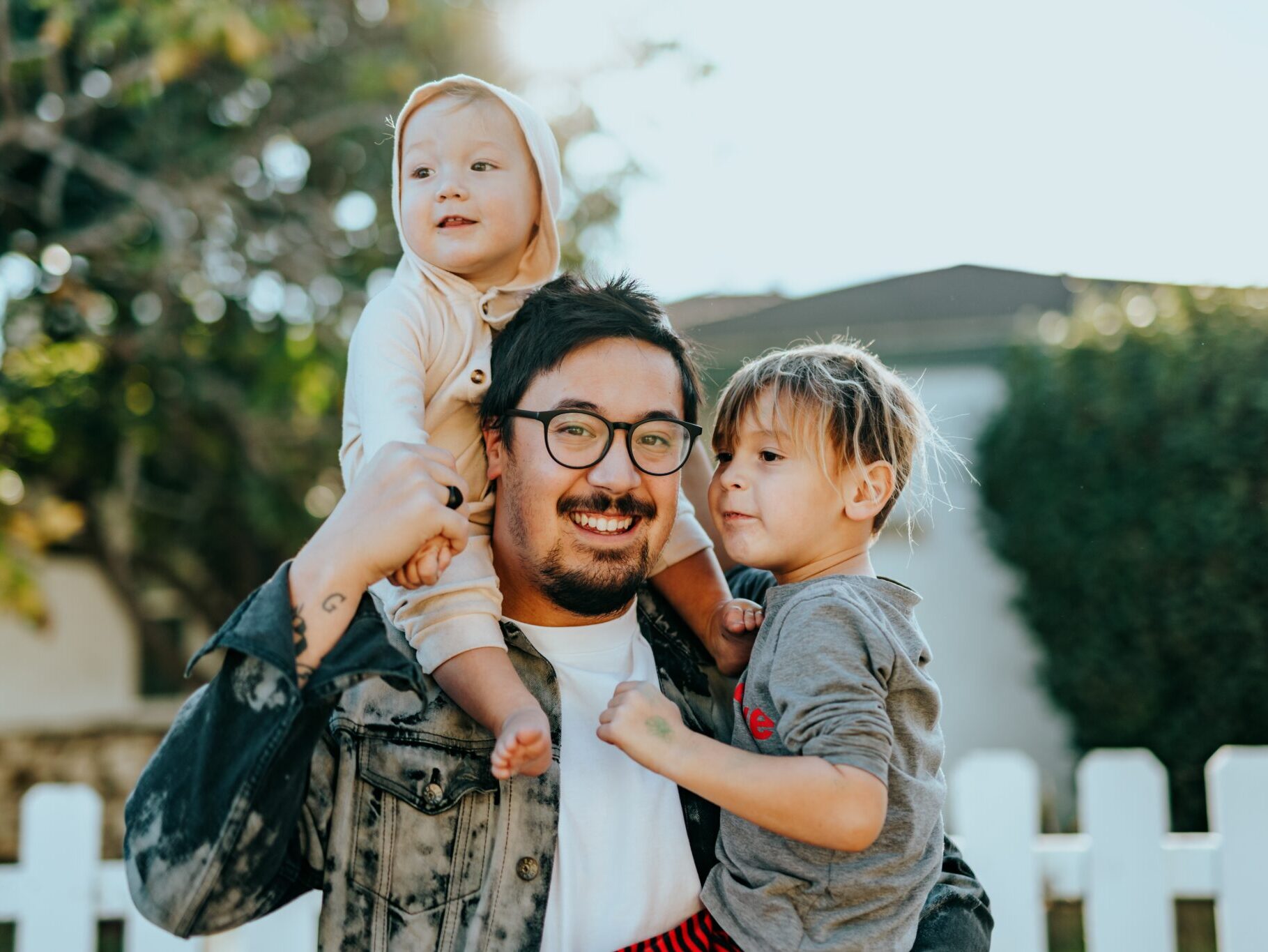 father, daughter and son posing in front of a white fence.