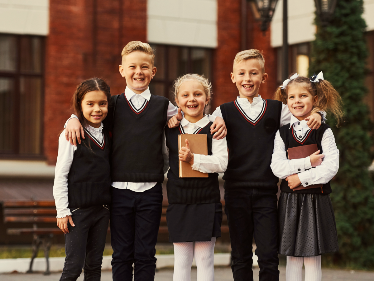 5 kids in school uniforms posing in front of school.