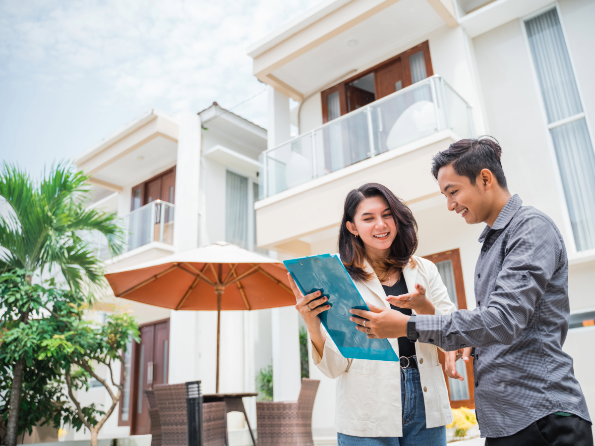 Realtor and client looking at clipboard with apartment/condo property behind them.