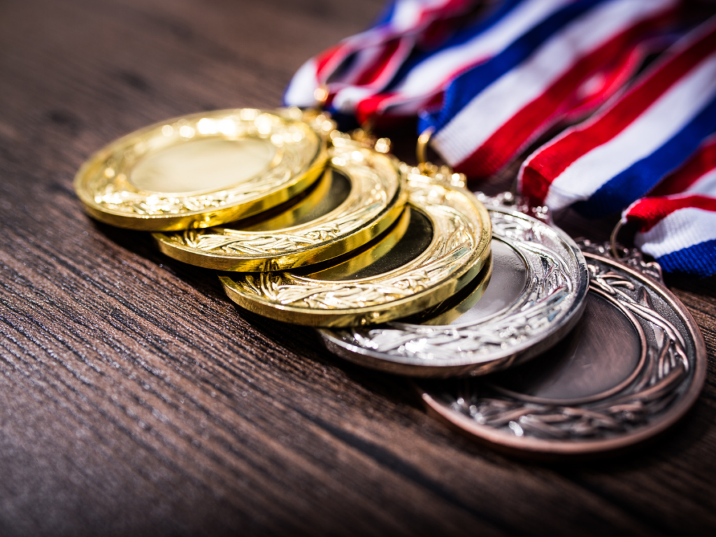 1st, 2nd, 3rd place medals stacked on table with red, white and blue ribbons attached.