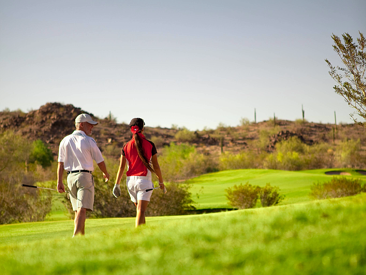 Estrella Golf Course with 2 people walking on green and hilly course away from camera.