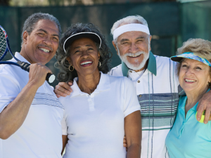 2 mixed pairs of senior friends posing for photo with tennis gear on and a tennis racket.