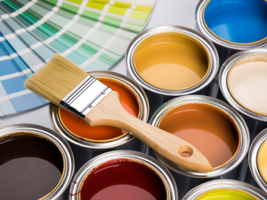 Paint cans with different colors and a paint brush sitting on top of them and paint chips of color in background.