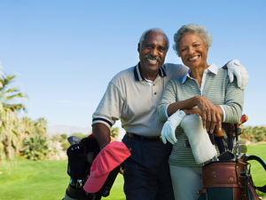 Senior couple standing together on golf course - man has his arm around woman - resting their arms on their golf bags.