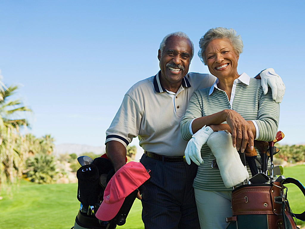 Senior couple standing together on golf course - man has his arm around woman - resting their arms on their golf bags for article on golf courses in Phoenix for newcomers and retirees moving to Phoenix.