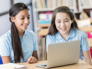 2 girls in school uniforms working on a laptop in library classroom for article 10 Impressive Private Schools In Phoenix for newcomers moving to Phoenix.