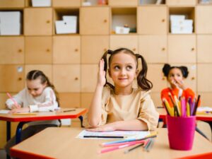 3 girls sitting at desks in school and the girl in front seat is raising her hand for article Top Public Schools in Phoenix Arizona for newcomers moving to Phoenix.