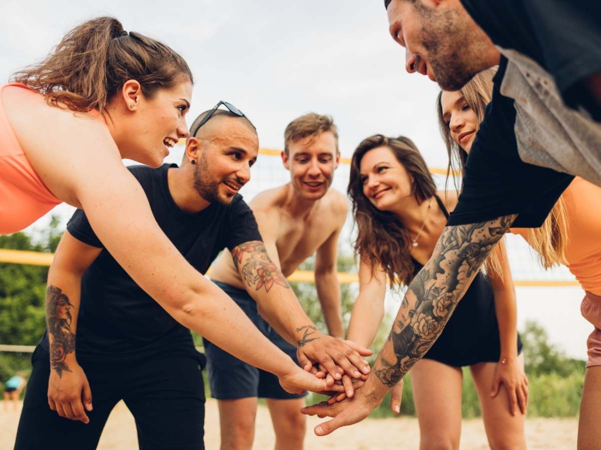 Group of people playing volleyball in a circle with hands in center for article Make Friends in Phoenix: 7 Easy Ways Without Awkwardness for newcomers moving to Phoenix.