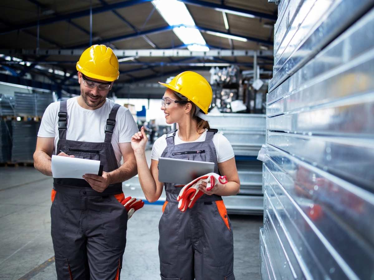 Male and female walking in plant with yellow hard hats and overalls on talking and taking notes for article Top Career Fields in Phoenix for Newcomers in 2025 moving to Phoenix.