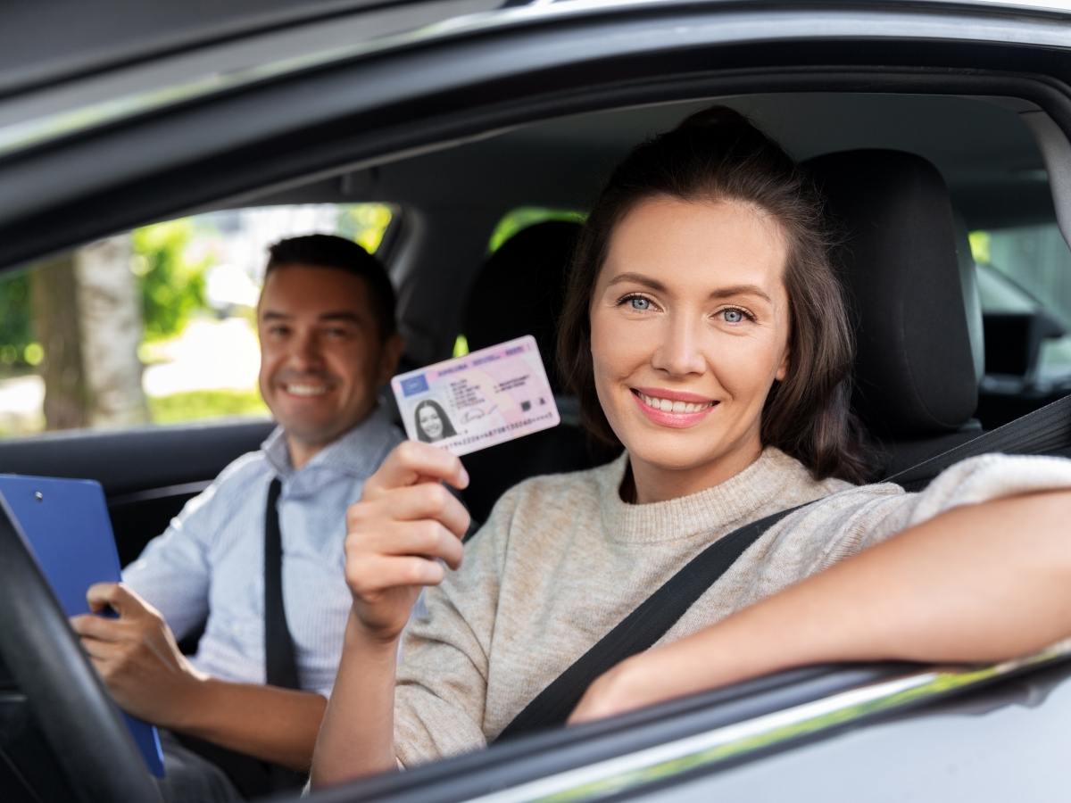Woman sitting in drivers seat of car holding up drivers license and smiling for article How to Change Your Driver’s License and Register Your Car in Phoenix