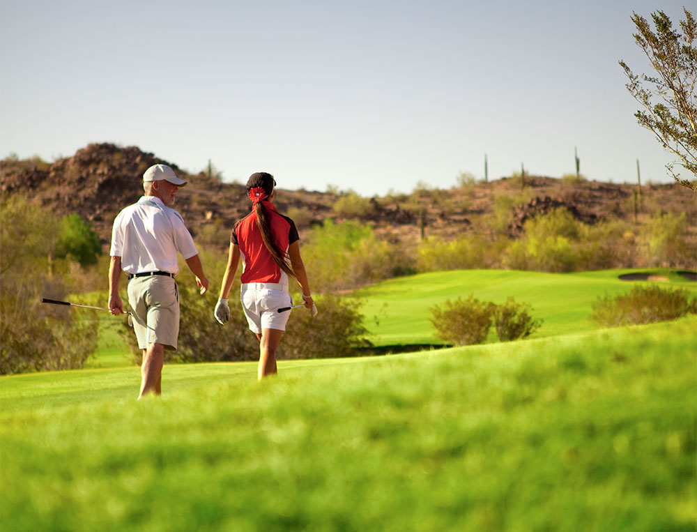 Man and girl walking up a green on a golf course on a sunny day