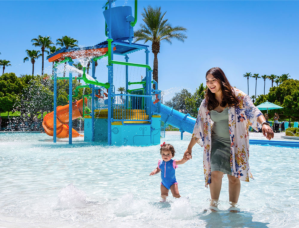 Mom with her toddler daughter walking in the water at a waterpark on a sunny day