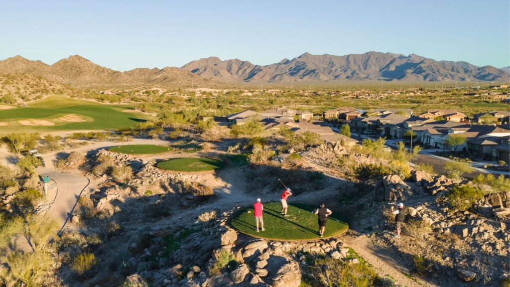 Guys playing golf in AZ hitting a ball off a tee in the sunset