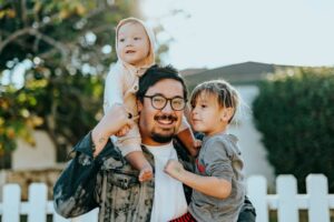 father, daughter and son posing in front of a white fence.