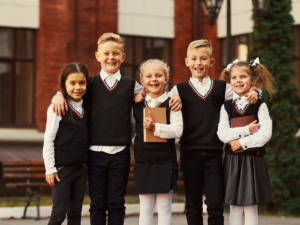 5 kids in school uniforms posing in front of school.